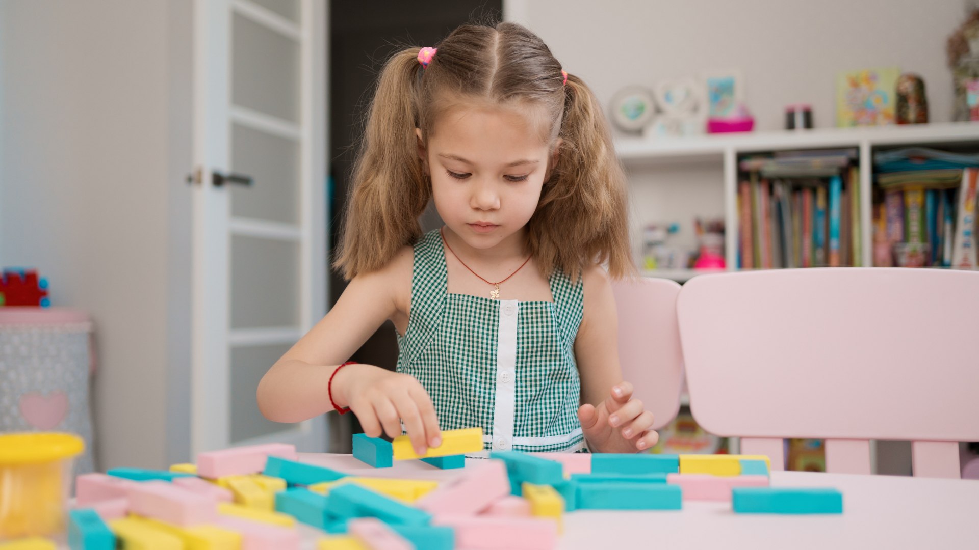 Kislány színes mágneses építőkockákkal játszik az asztalon, koncentrál a kreatív építésre a gyerekszobában.