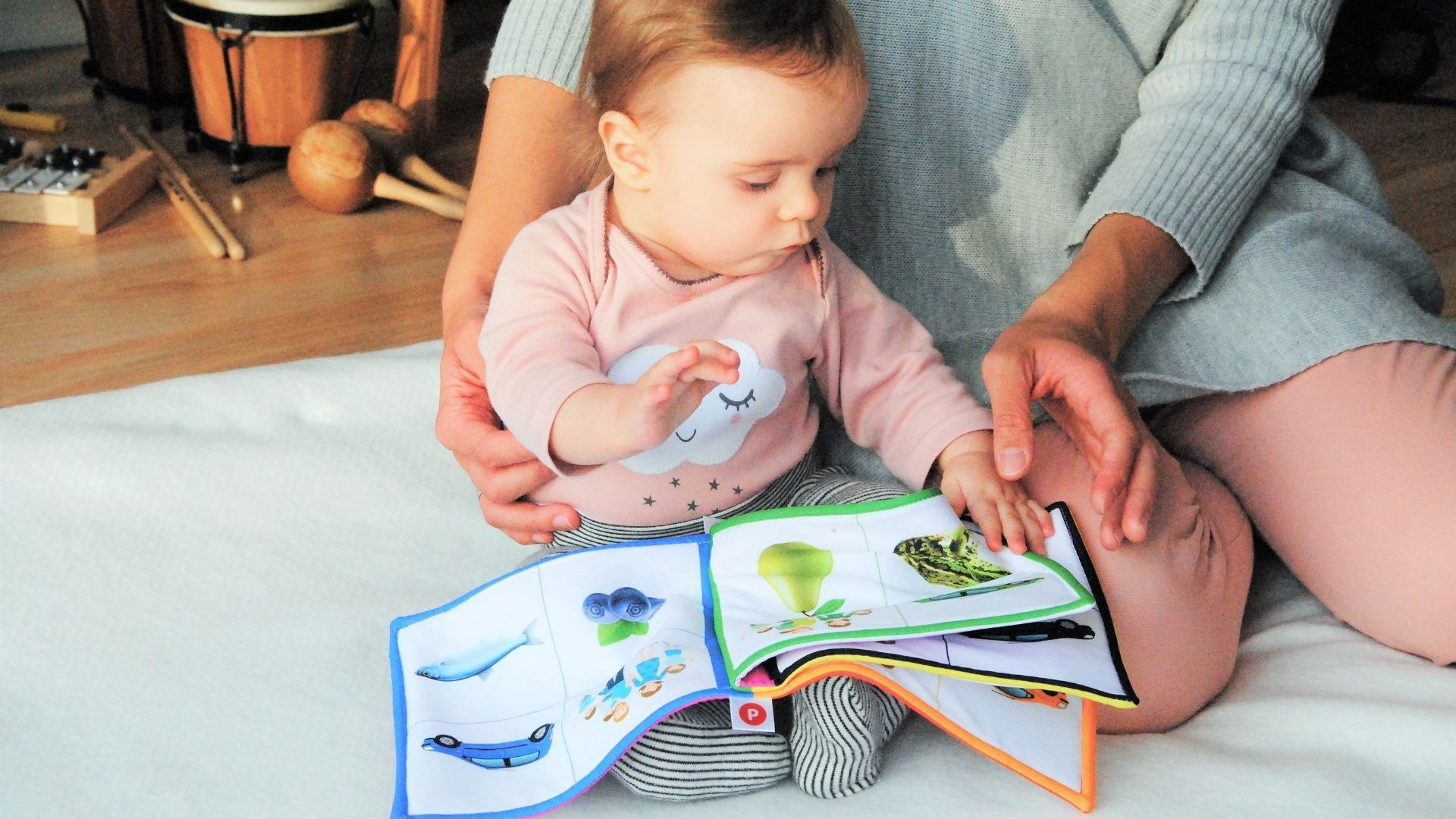 Baba textilkönyv lapját fogja a játszószőnyegen